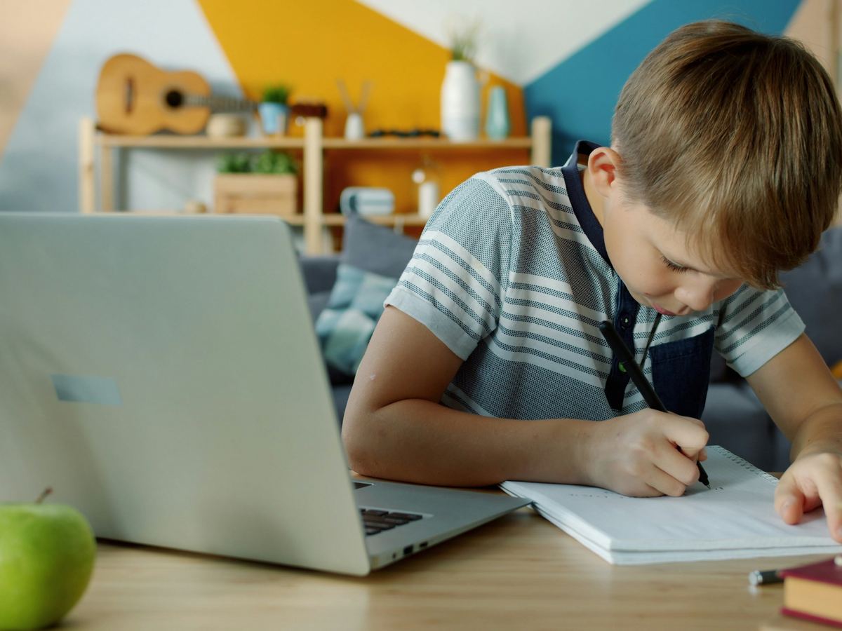 ノートパソコンの前で、ノートに書き込みながら勉強する小学生
